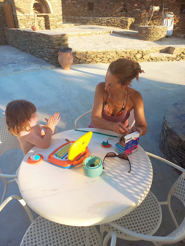 Babysitter engaging a young child with educational toys at an outdoor table in Sifnos