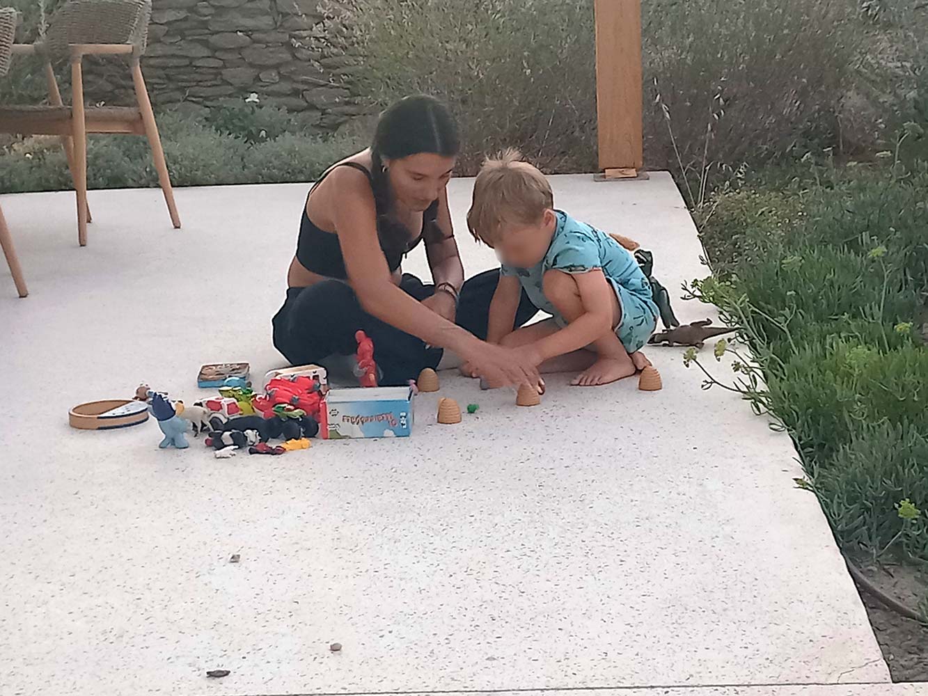 Babysitter assisting a toddler with a hands-on learning game during outdoor playtime